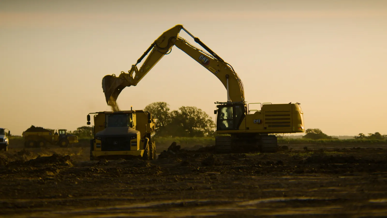 An excavator loading an articulated dump truck — supplied in Bedrock Robotics’ public media kit; the kit does not identify whether this machine carries the autonomy fit-out. Photo: Bedrock Robotics